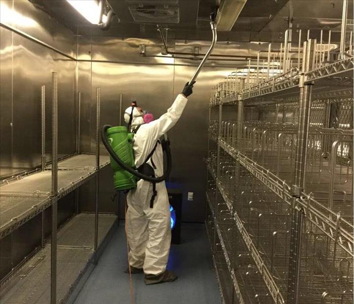 Servpro technician suited in ppe vacuuming in a silver supply room.